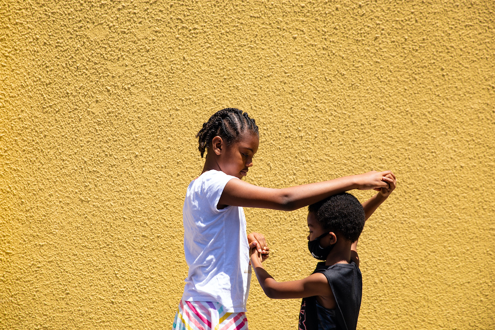  Amaya Johnson (left) and DeShonno Johnson Jr. play nearby as cars are decorated in preparation for a graduation parade through the 54th District in Los Angeles on June 13, 2020. Alexis Hunley for *New York* magazine.