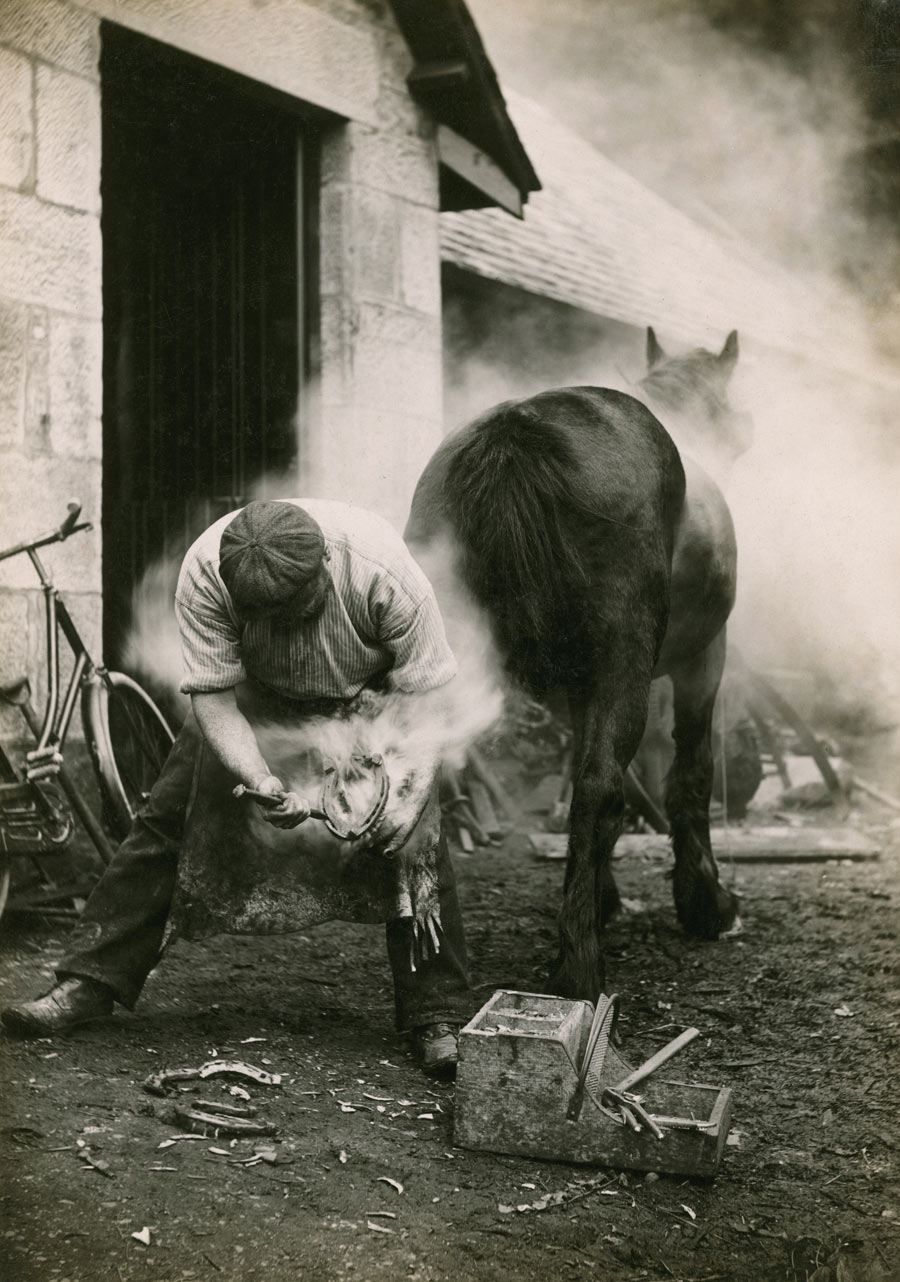 A farmer buring the hoof of a horse before shoeing it in Scotland, May 1921. Photograph by William Reid, National Geographic